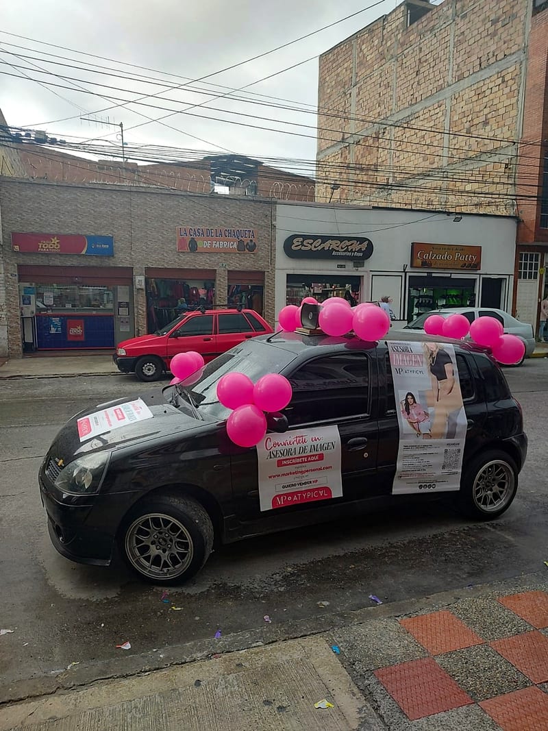 Carro de perifoneo con globos rosados frente a locales comerciales